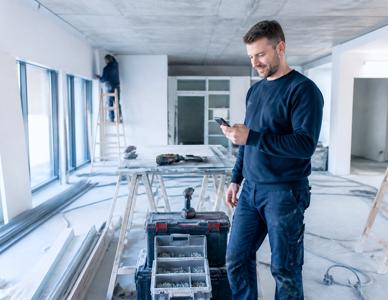 Handwerker nutzt sein Smartphone zur mobilen Leistungserfassung auf einer Baustelle.